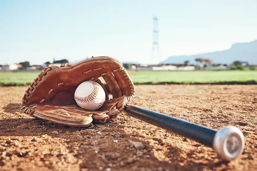 A baseball glove, bat, and ball on a baseball field after training lessons for hitting, pitching, catching, and fielding.